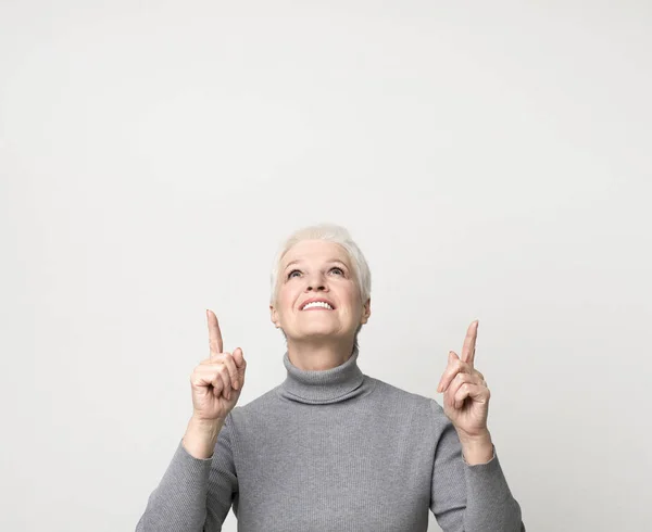 Great offer. Beautiful senior woman pointing upwards at copy space — Stock Photo, Image