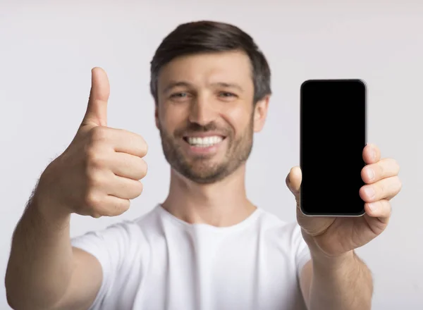 Un homme souriant tenant un téléphone cellulaire vide, les pouces levés, isolé — Photo