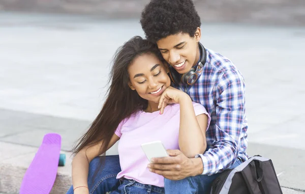 Estudantes sorridentes rolando fotos no smartphone juntos sentados ao ar livre — Fotografia de Stock