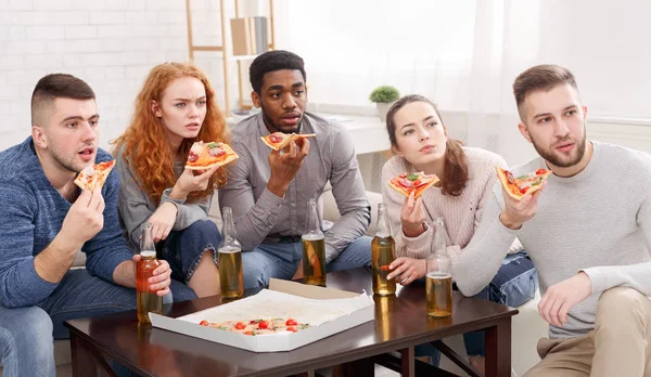Friends watching TV with surprise, eating pizza