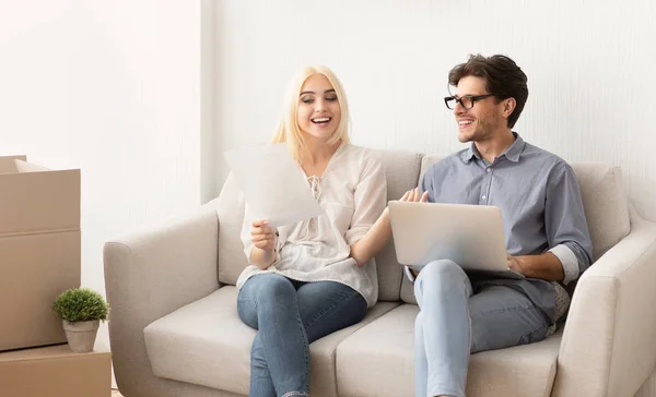 Pareja lectura certificado de propiedad sentado en el sofá utilizando el ordenador portátil — Foto de Stock