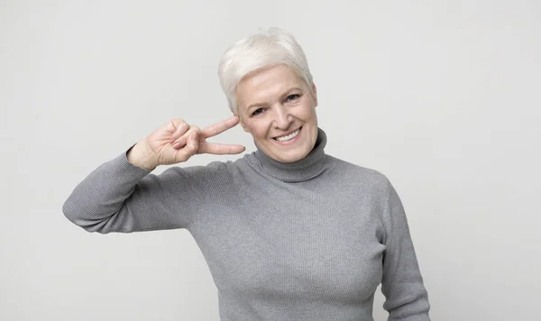 Idős hölgy mutatja v-jel béke gesztus, mosolyogva a kamera — Stock Fotó