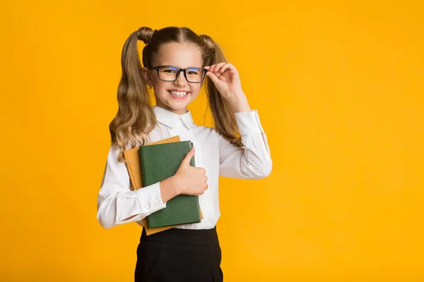 Felice scuola ragazza in possesso di libri su sfondo giallo, studio shot — Foto Stock