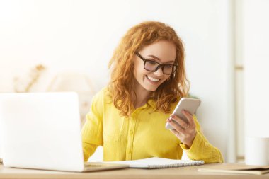 Ofis masasında çalışan ve cep telefonuyla mesaj laşmaya çalışan iş kadını