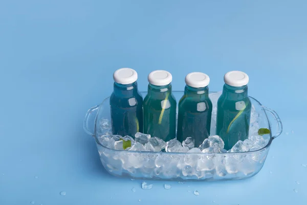 Μπλε νερό αποτοξίνωσης σε γυάλινες φιάλες με παγάκια στο παρασκήνιο — Φωτογραφία Αρχείου