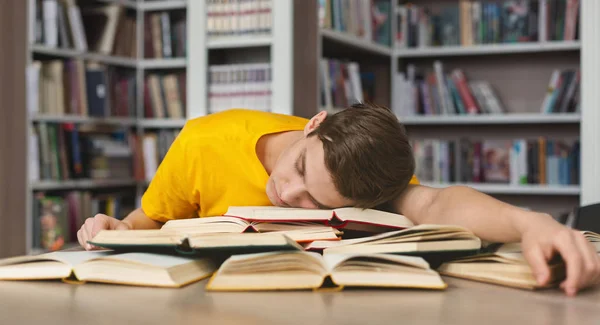 Trött kille tupplur på böcker i biblioteket — Stockfoto