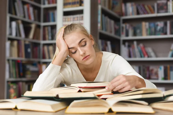 Уставшая блондинка читает книги в библиотеке — стоковое фото
