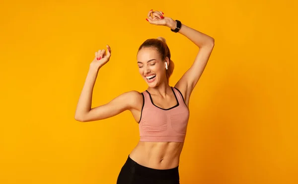 Aufgeregte junge Frau in Sportkleidung tanzt auf gelbem Hintergrund — Stockfoto