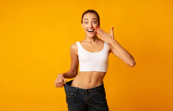 Emocionada chica posando en pantalones vaqueros de gran tamaño sobre fondo de estudio amarillo — Foto de Stock