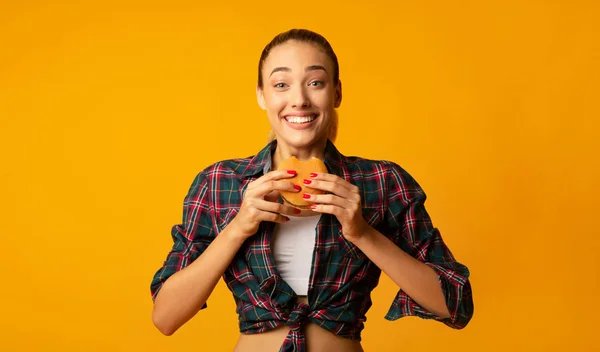 Slim Girl äta Burger över Yellow Studio bakgrund — Stockfoto