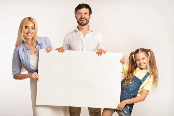 Familia feliz sosteniendo tablero en blanco sobre fondo blanco — Foto de Stock