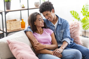 Evde kanepede oturan, birbirlerine sarılan gençler