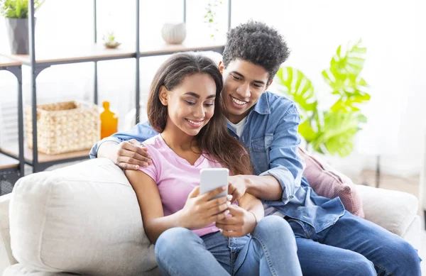 Sonriendo a los estudiantes desplazando fotos en el teléfono inteligente juntos sentados en casa — Foto de Stock