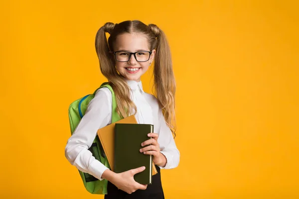 Uśmiechnięta Szkoła podstawowa dziewczyna trzyma książki stwarzające na żółtym tle — Zdjęcie stockowe