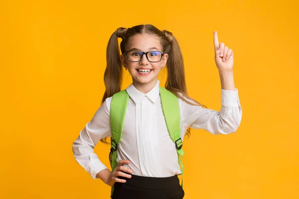 Glimlachend nerdy schoolmeisje wijzend vinger omhoog met idee, gele achtergrond — Stockfoto