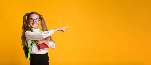 Adorabile studentessa che punta il dito al libro contenente copyspace, sfondo giallo — Foto Stock