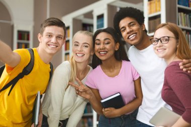 Mutlu uluslararası üniversite öğrencileri kütüphanede selfie çekiyor