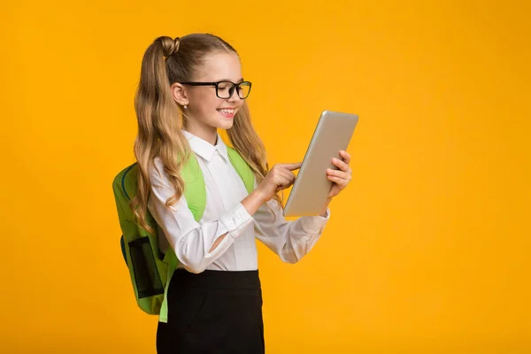 Sorridente scuola elementare ragazza utilizzando tavoletta digitale su sfondo giallo — Foto Stock