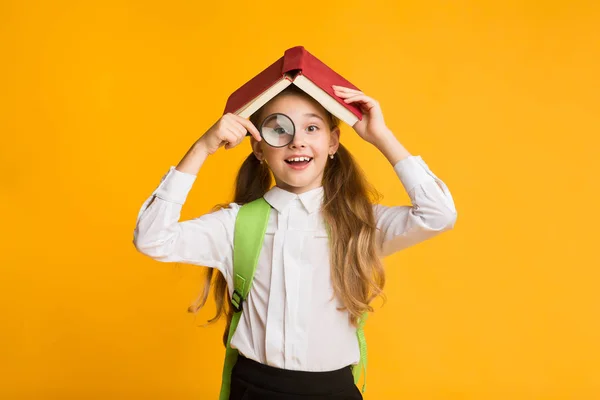 Carino curioso studentessa guardando attraverso lente di ingrandimento copertura testa con libro — Foto Stock