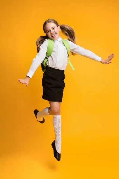 Opgewonden kleine schoolmeisje springen over gele studio achtergrond. — Stockfoto