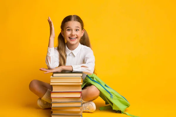Okos iskoláslány emelés kézi ülő-on könyv boglya, sárga háttér — Stock Fotó