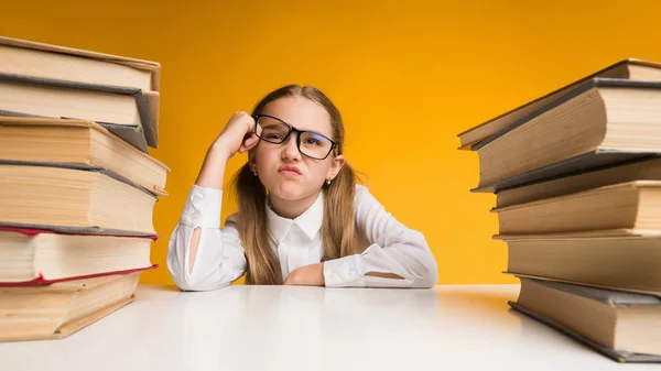 Scontento scuola primaria ragazza seduta tra libro stack su giallo — Foto Stock