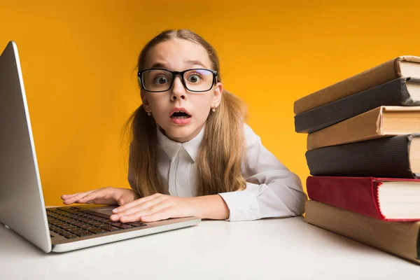 Überraschte Erstklässlerin bei Hausaufgaben auf Laptop, gelber Studiohintergrund — Stockfoto