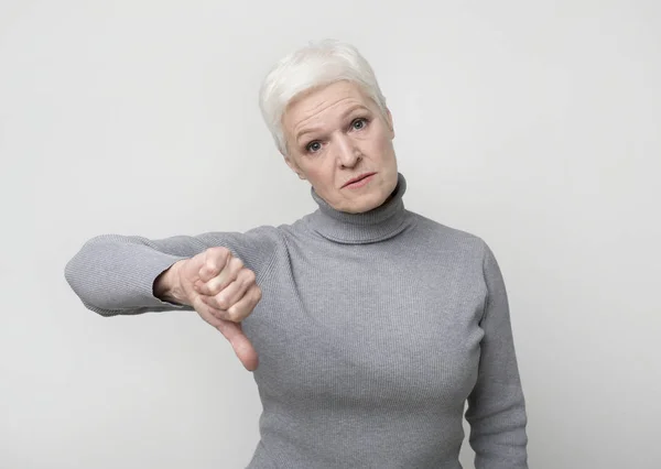 Расстроенная пожилая женщина показывает большой палец вниз жест как символ отказа — стоковое фото