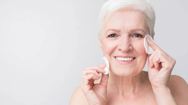 Charmante Senior vrouw het reinigen van haar gezicht met katoenen pads — Stockfoto