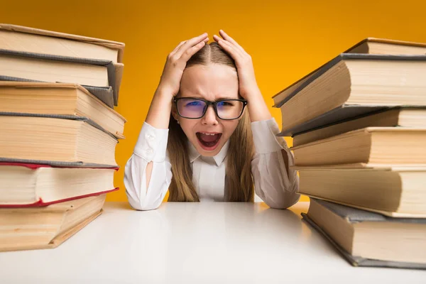 Assustado escola menina gritando embreagem cabeça sentado entre livro pilhas — Fotografia de Stock