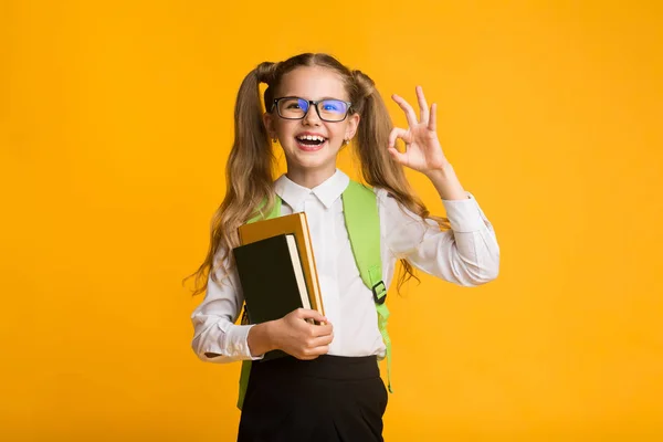 可爱的一年级女学生手势确定在黄色背景的相机 — 图库照片