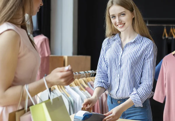 Asistente de tienda sonriendo mientras pasa la tarjeta de crédito en la tienda de ropa — Foto de Stock