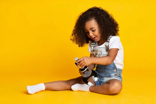 Bambina che gioca con il microscopio, sfondo giallo — Foto Stock