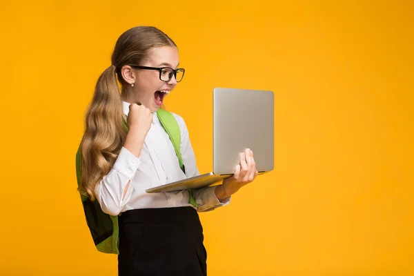 Opgewonden schoolmeisje spelen computer spelletjes op laptop over gele achtergrond — Stockfoto