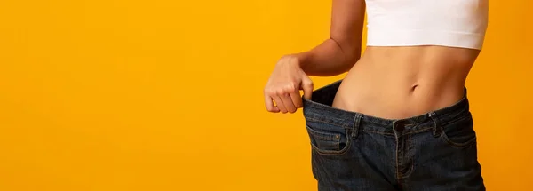 Женщина показывает огромные джинсы после потери веса на желтом фоне — стоковое фото
