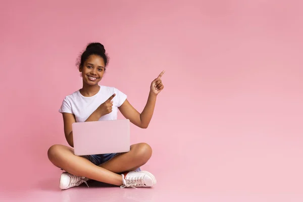 Aufgeregtes Teenager-Mädchen mit Laptop zeigt auf rosa Hintergrund — Stockfoto