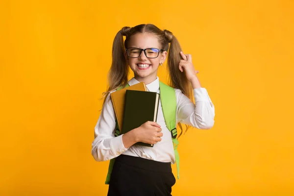 Bonito estudante de primeira classe menina mantendo os dedos cruzados no fundo amarelo — Fotografia de Stock