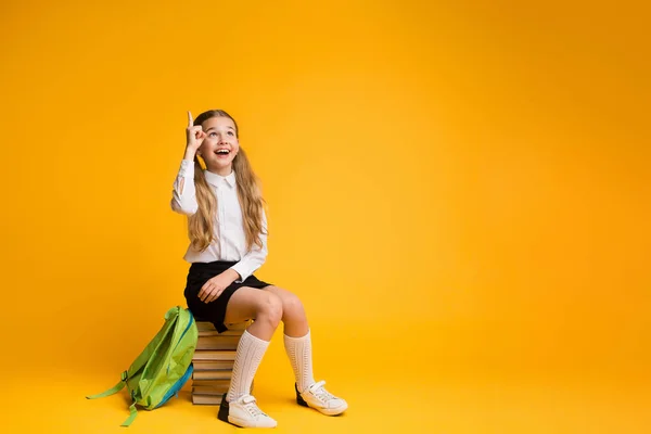 Okos általános iskola lány mutatva ujját felfelé ül stack könyvek — Stock Fotó