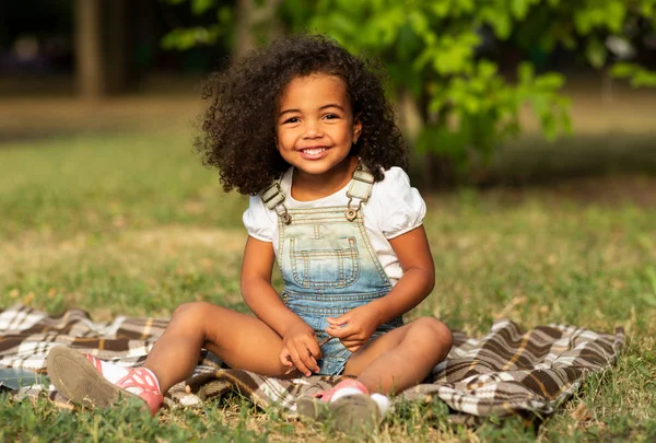 Menina bonito feliz sentado em cobertor na natureza — Fotografia de Stock