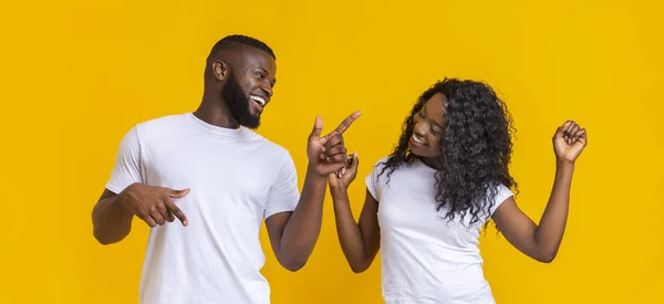 Joyful african american couple dancing on yellow studio background