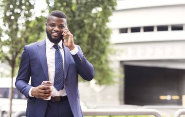 Resmi takım elbiseli milenyum adamı kahve içiyor ve cep telefonu kullanıyor.