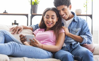 Bin yıllık siyah çift birlikte kanepede oturan akıllı telefon kullanarak