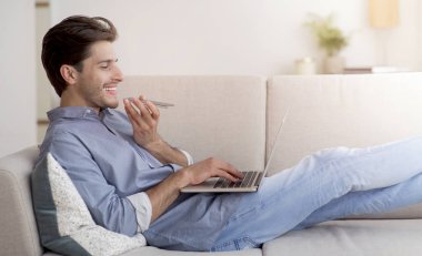 Kanepede Yatan Dizüstü Bilgisayar Kullanarak Telefonda Konuşan Neşeli Adam