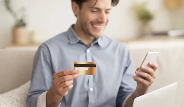 Guy holding credit card and using mobile phone at home — Stock Photo, Image