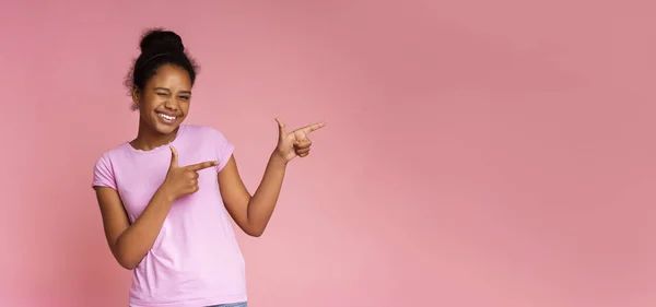 Verspieltes Mädchen zwinkert und zeigt mit zwei Fingern auf Kopierraum — Stockfoto