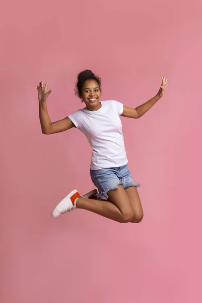 Pozytywne African American Girl skoki nad różowe Studio tle — Zdjęcie stockowe