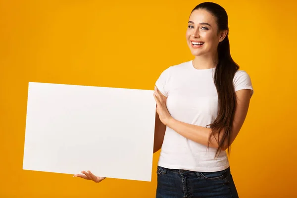 Vrolijke dame houdt blanco bord voor tekst op gele achtergrond — Stockfoto