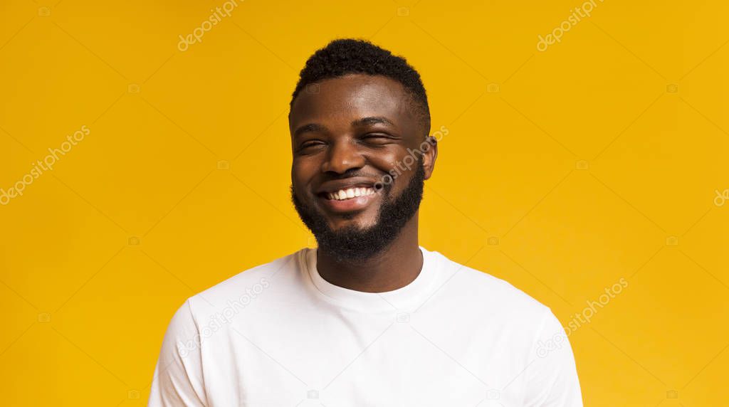 Cute carefree black guy laughing on yellow studio background
