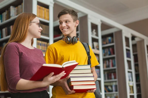 Bonito casal adolescente discutindo livro na biblioteca — Fotografia de Stock
