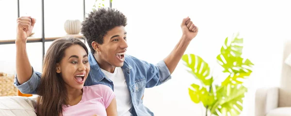 Goal. Euphoric black teenage couple watching football at home